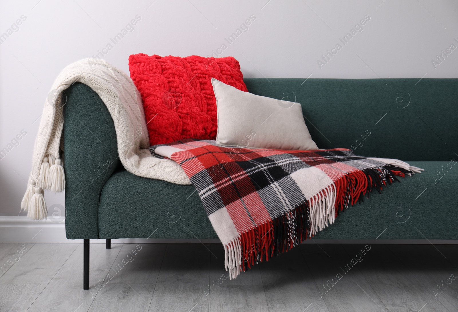 Photo of Sofa with soft pillows and warm plaids near light wall indoors