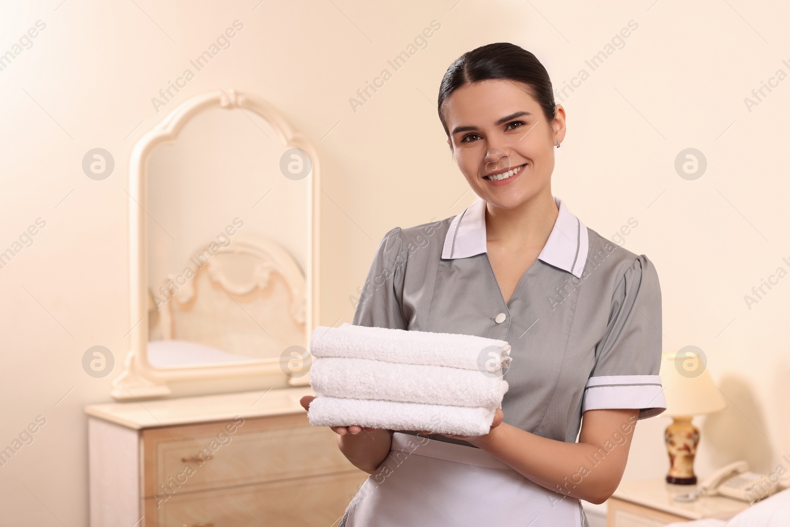 Photo of Young chambermaid holding stack of clean towels in hotel room. Space for text