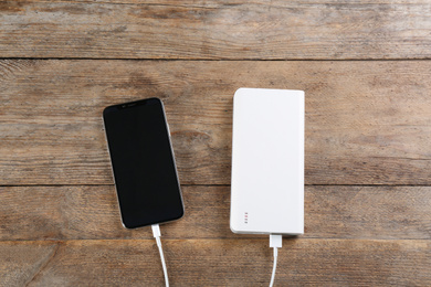 Photo of Mobile phone charging with power bank on wooden background, flat lay