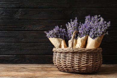 Fresh lavender flowers in basket on wooden table against dark background, space for text