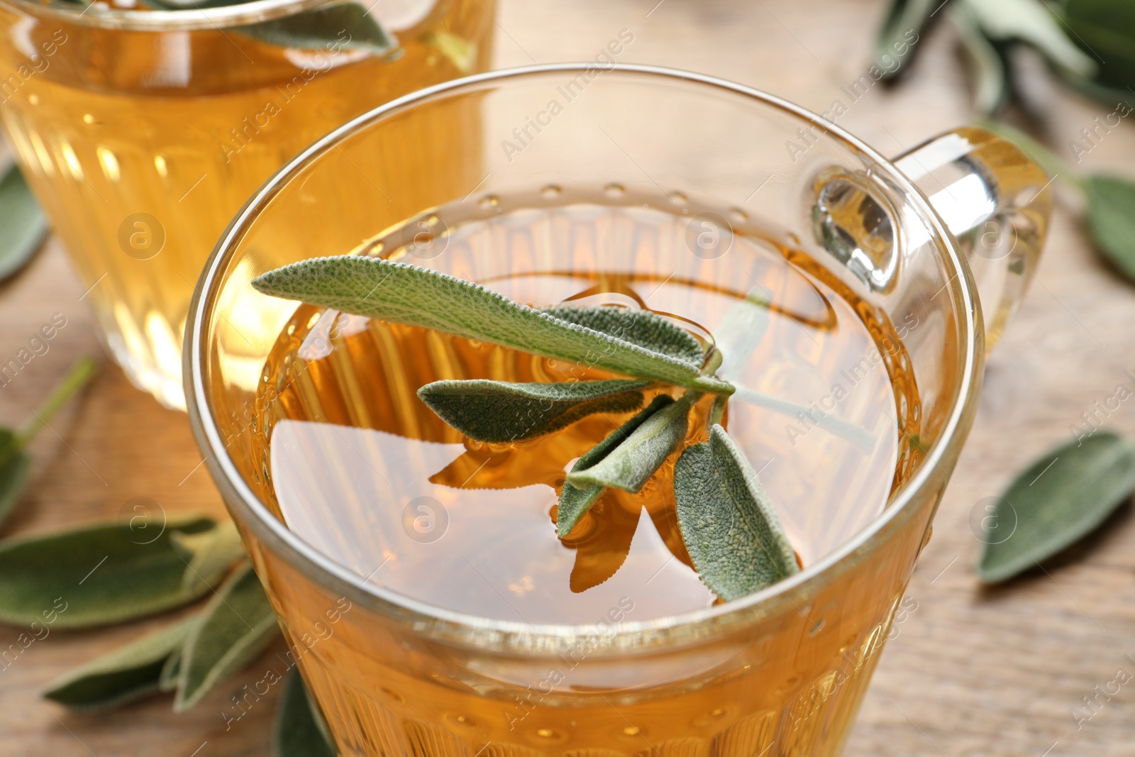 Photo of Cup of aromatic sage tea with fresh leaves on table, closeup