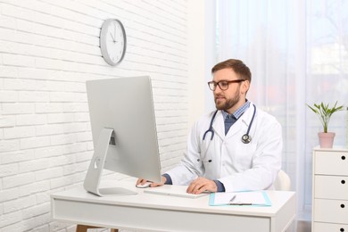 Pediatrician consulting patient online at table in clinic