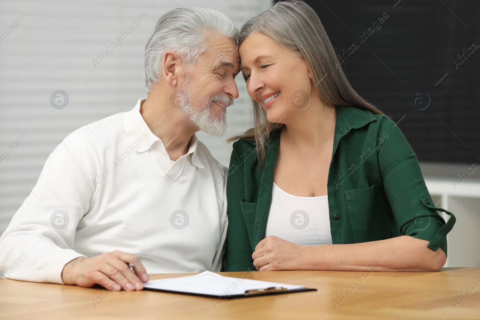 Photo of Happy senior couple signing Last Will and Testament indoors