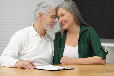 Happy senior couple signing Last Will and Testament indoors