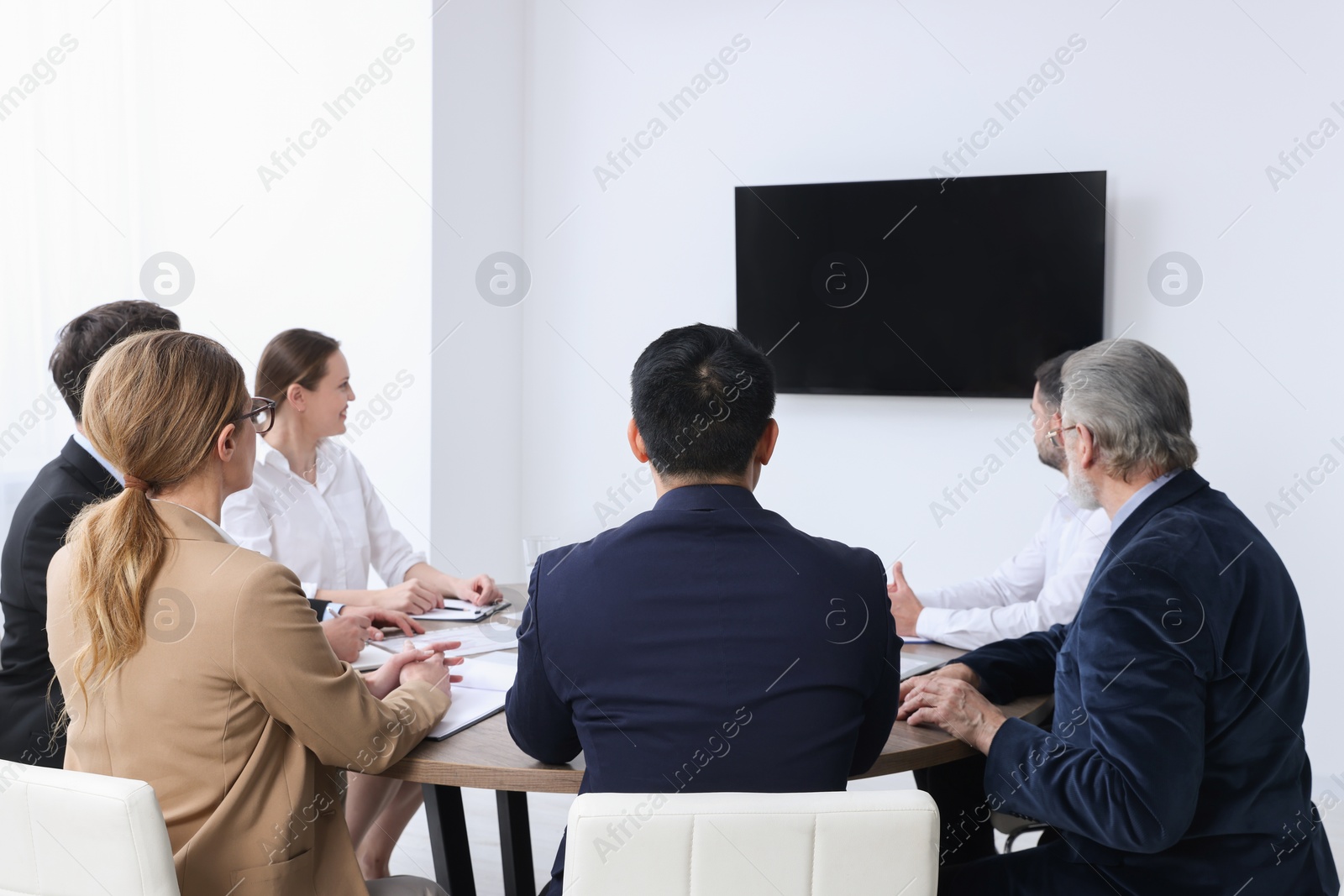 Photo of Business conference. Group of people watching presentation on tv screen in meeting room