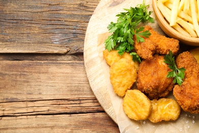 Tasty nuggets and deep fried chicken pieces with garnish on wooden table, top view. Space for text