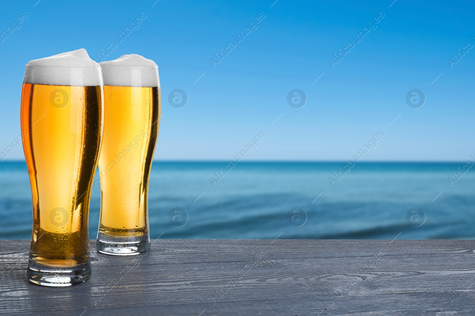 Image of Cold beer on wooden desk against blurred sea. Space for text