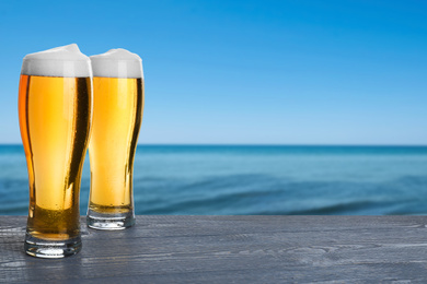 Image of Cold beer on wooden desk against blurred sea. Space for text