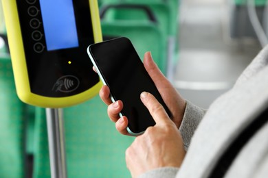 Photo of Woman with smartphone near contactless fare payment device in public transport, closeup
