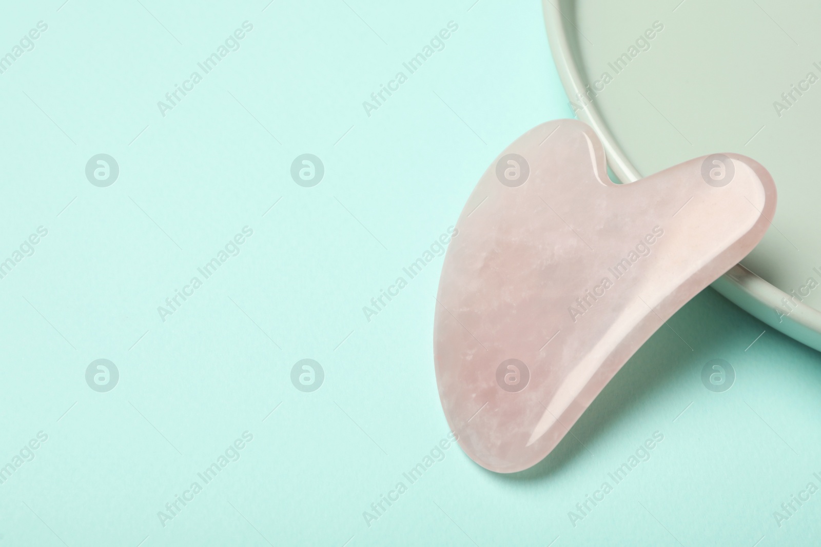 Photo of Rose quartz gua sha tool on turquoise background, space for text