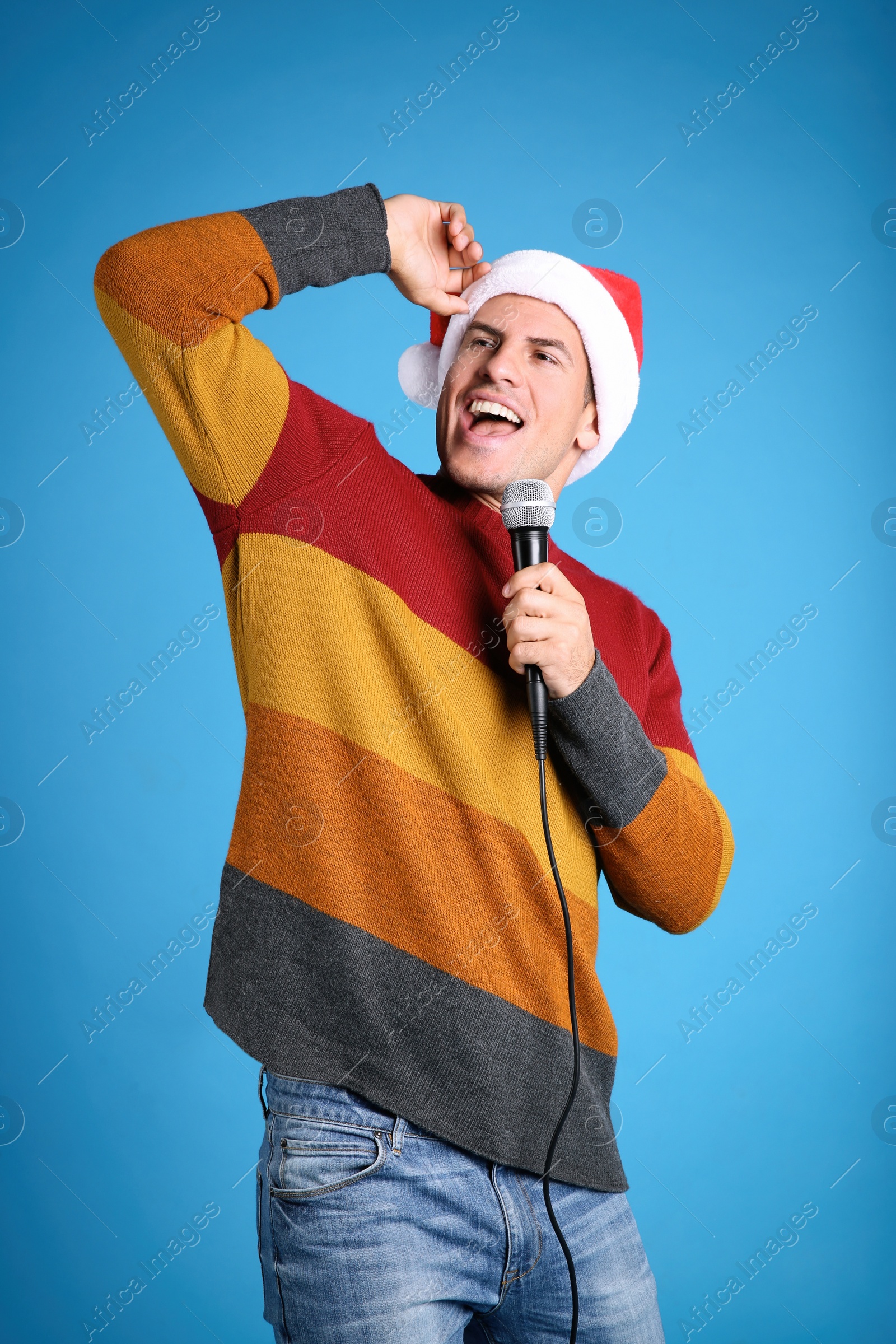 Photo of Emotional man in Santa Claus hat singing with microphone on blue background. Christmas music