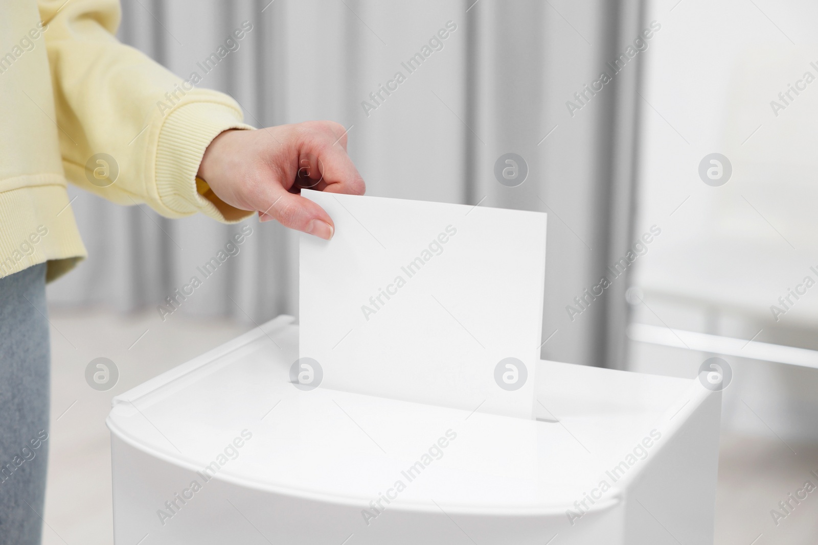 Photo of Woman putting her vote into ballot box on blurred background, closeup