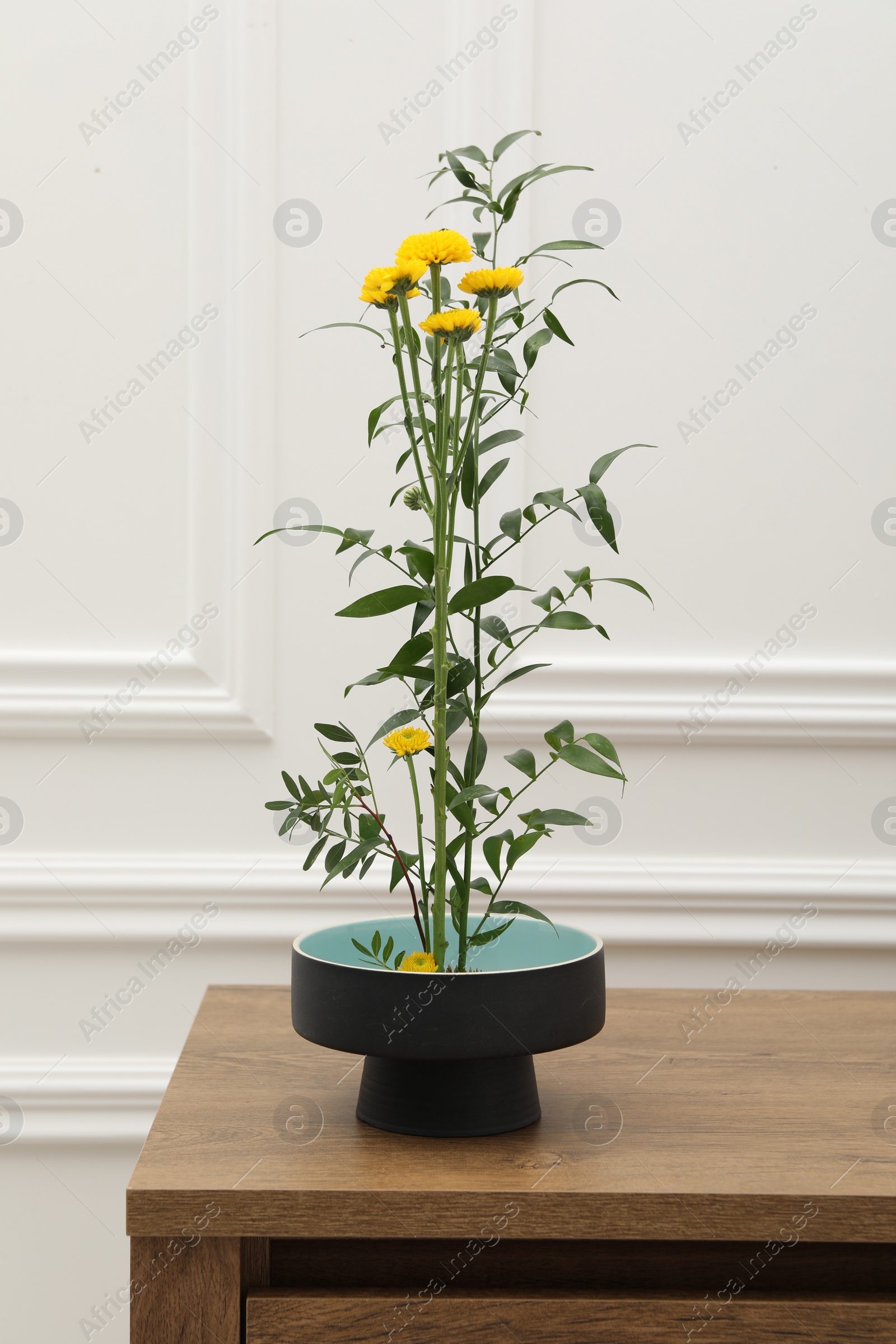 Photo of Ikebana art. Beautiful yellow flowers and green branch carrying cozy atmosphere at home