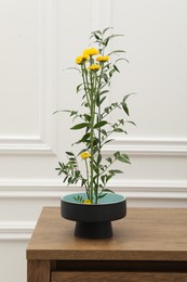 Photo of Ikebana art. Beautiful yellow flowers and green branch carrying cozy atmosphere at home