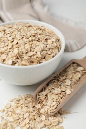 Bowl and scoop with oatmeal on white wooden table, closeup