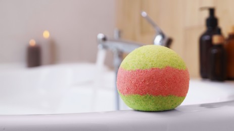 Photo of Colorful bath bomb on white tub in bathroom. Space for text