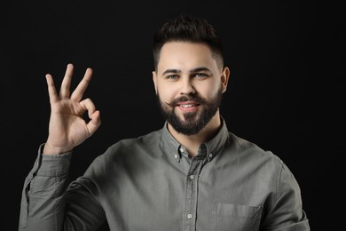 Photo of Young man with mustache showing OK gesture on black background