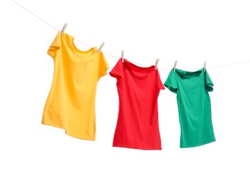 Different bright t-shirts drying on washing line against white background