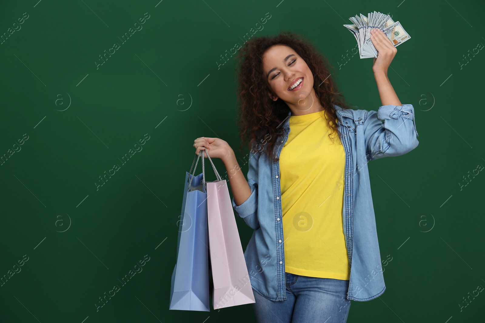 Photo of Young African-American woman with money and shopping bags on color background. Space for text