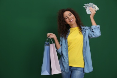 Young African-American woman with money and shopping bags on color background. Space for text