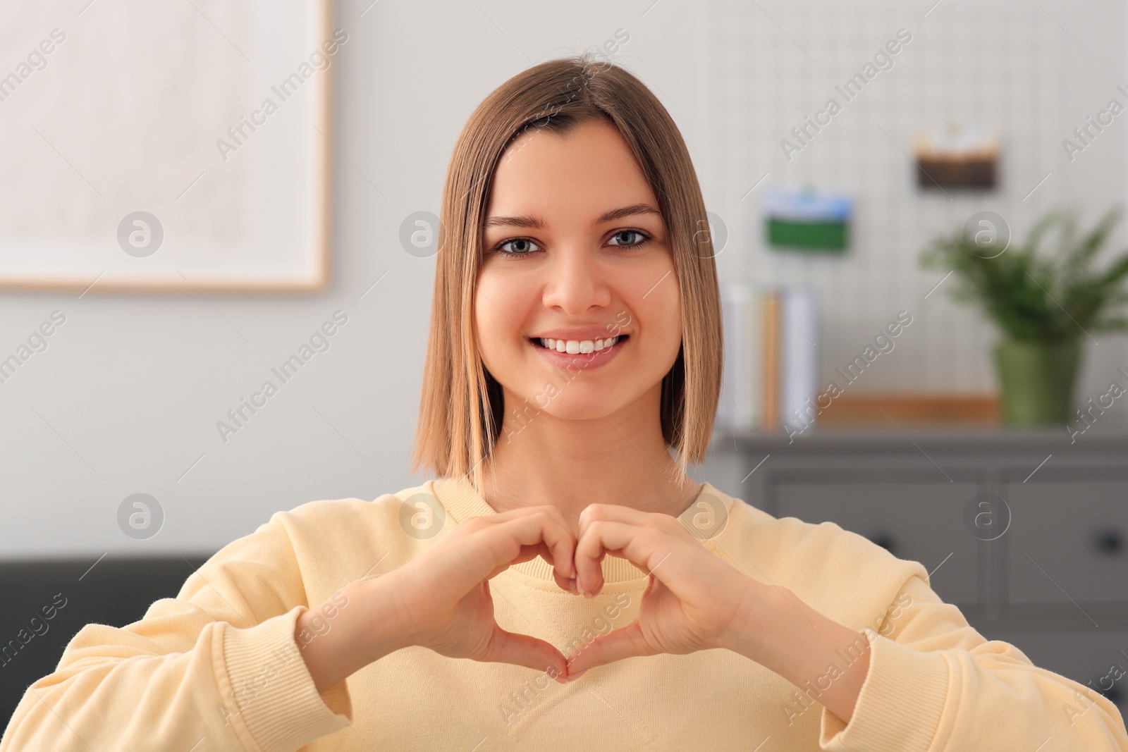 Photo of Young woman making heart with hands indoors. Volunteer concept