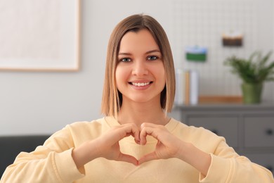 Young woman making heart with hands indoors. Volunteer concept