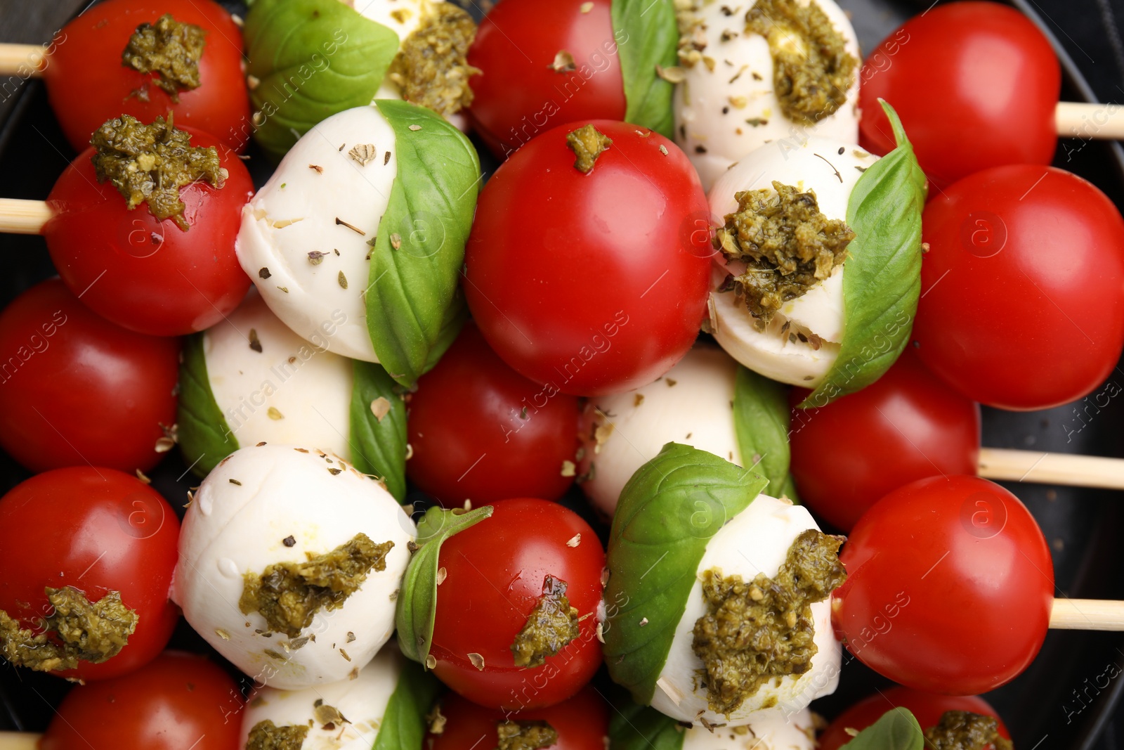 Photo of Caprese skewers with tomatoes, mozzarella balls, basil and pesto sauce, top view