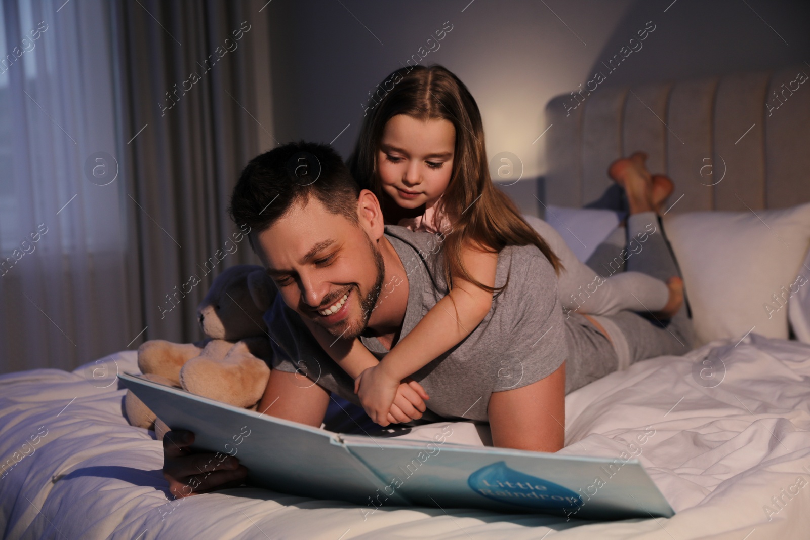 Photo of Father with his daughter reading book in bed at home