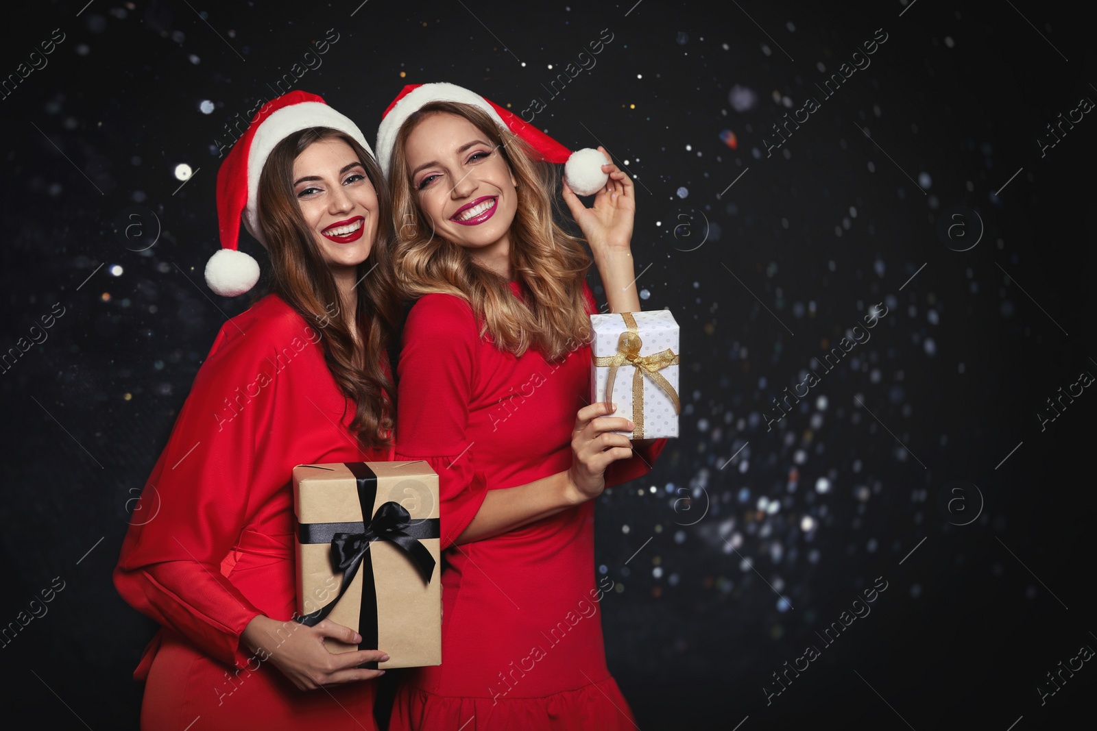 Photo of Happy women in Santa hats with gift boxes on black background, space for text. Christmas party