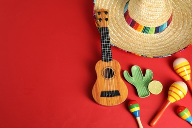 Photo of Flat lay composition with Mexican sombrero hat and ukulele on red background. Space for text