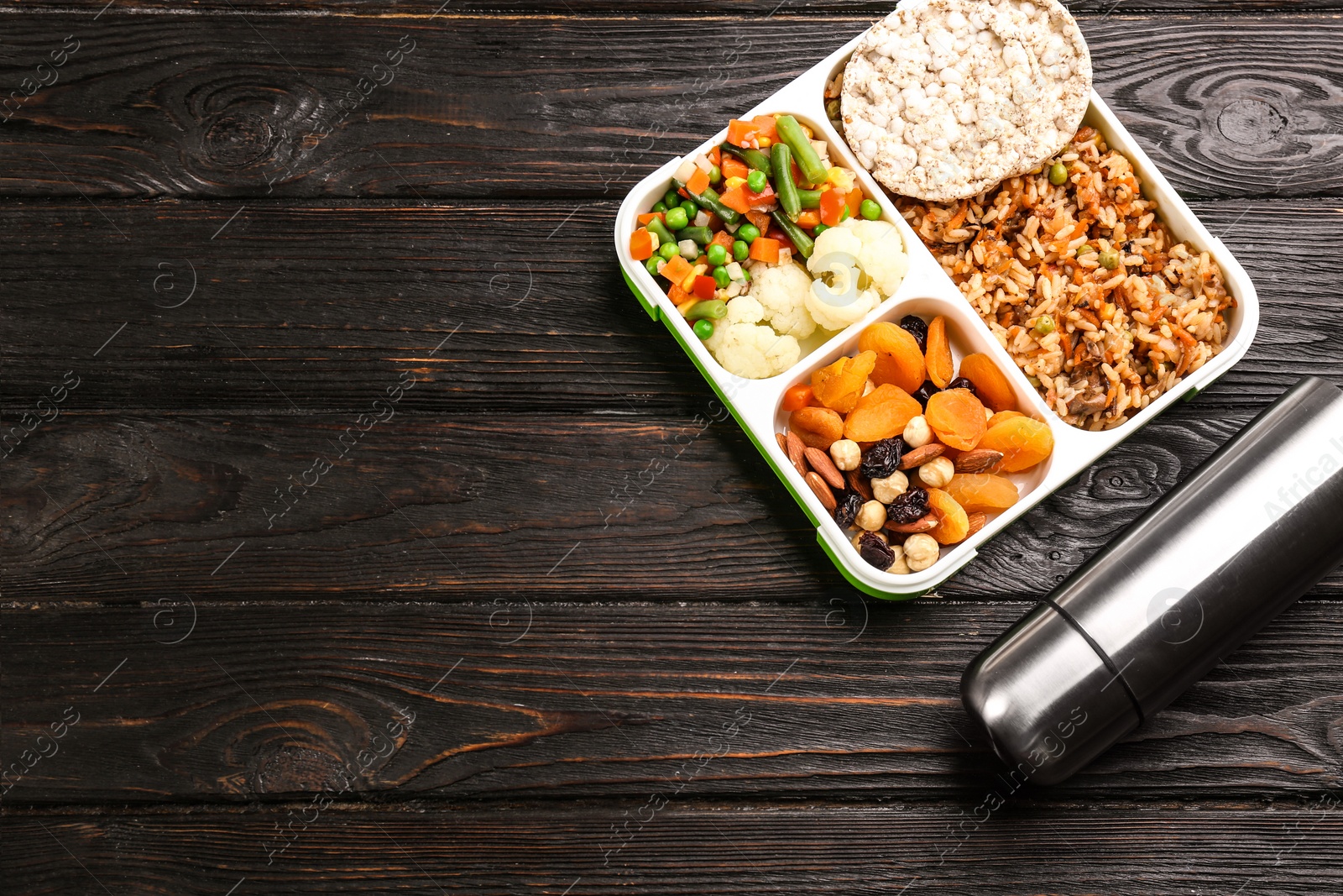 Photo of Thermos bottle and lunch box with food on black wooden background, flat lay. Space for text