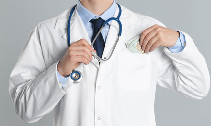 Doctor putting bribe into pocket on grey background, closeup. Corruption in medicine