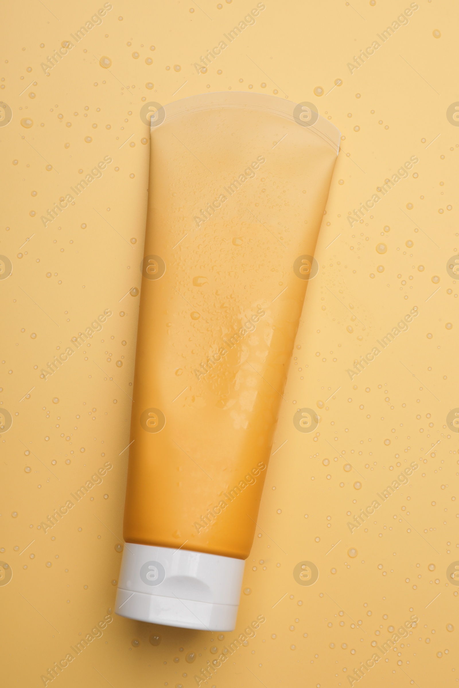 Photo of Wet tube of face cleansing product on pale orange background, top view