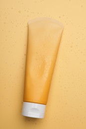 Wet tube of face cleansing product on pale orange background, top view