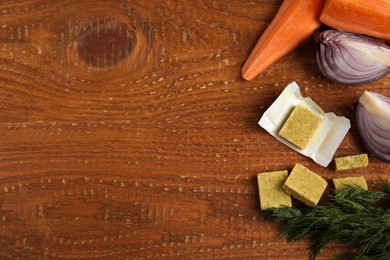 Photo of Bouillon cubes and other ingredients on wooden table, flat lay. Space for text