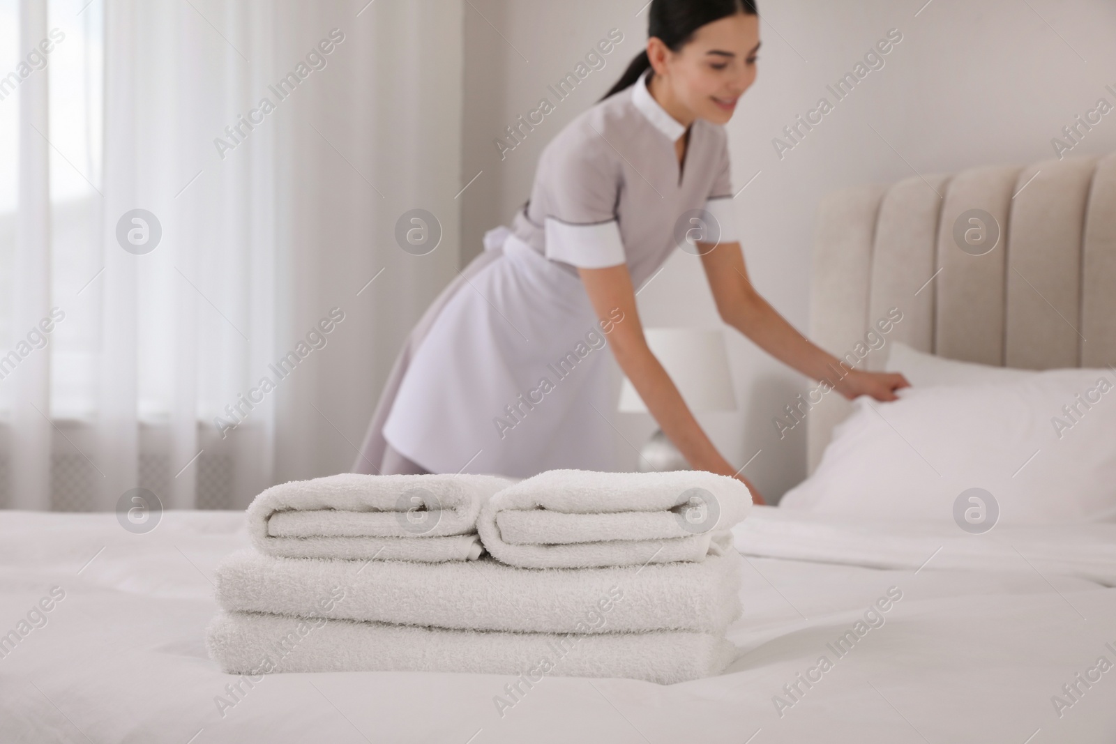 Photo of Chambermaid making bed in hotel room, focus on fresh towels. Space for text