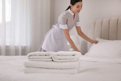Chambermaid making bed in hotel room, focus on fresh towels. Space for text