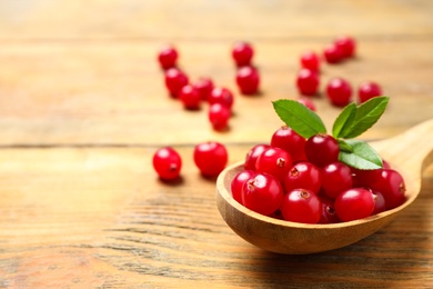 Photo of Spoon with tasty cranberries and green leaves on wooden table, closeup. Space for text