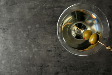 Photo of Glass of Classic Dry Martini with olives on grey table, top view. Space for text
