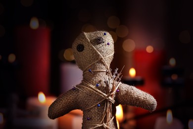 Image of Voodoo doll with pins and dried flowers in dark room, closeup. Curse ceremony