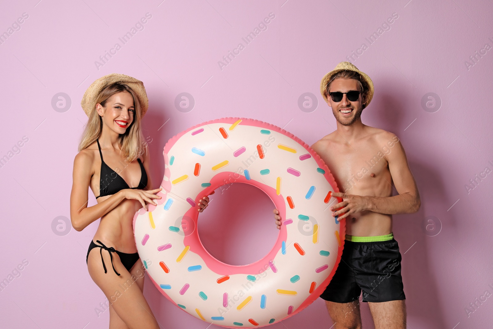 Photo of Happy young couple in beachwear with inflatable ring on color background