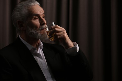 Senior man in suit drinking whiskey on brown background. Space for text