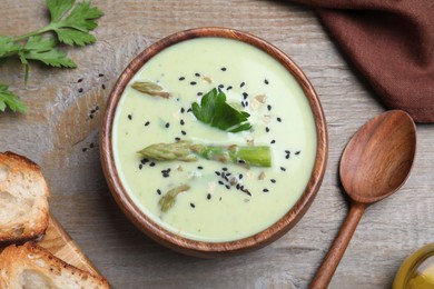 Photo of Bowl of delicious asparagus soup served on wooden table, flat lay