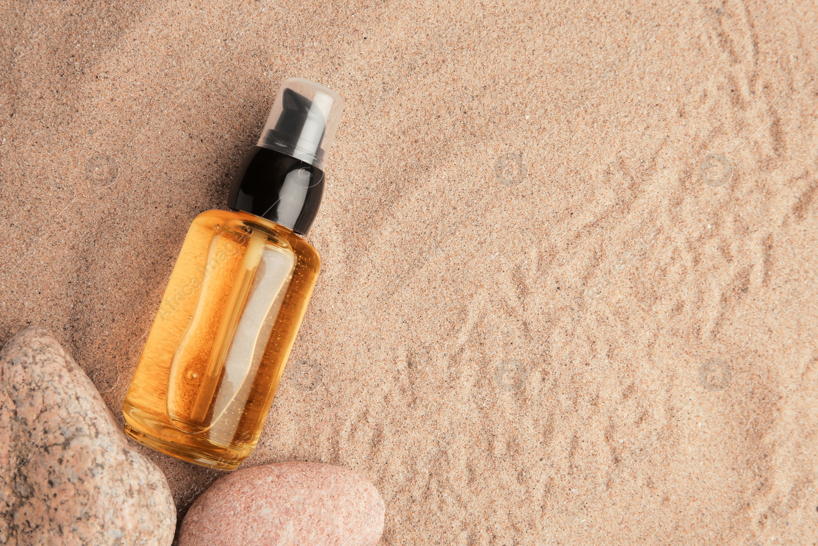 Photo of Bottle of serum and stones on sand, flat lay. Space for text