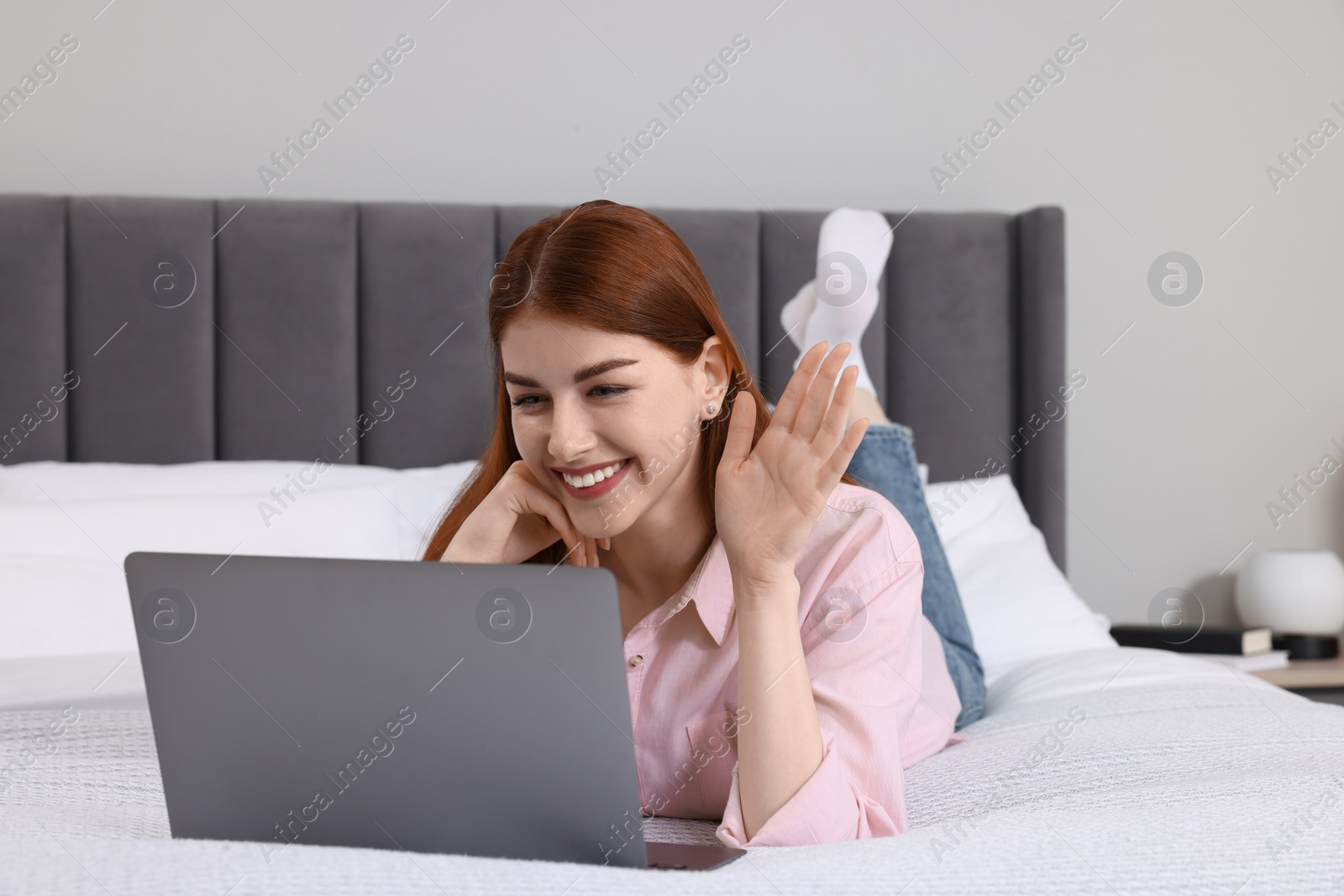 Photo of Happy woman having video chat via laptop on bed in bedroom