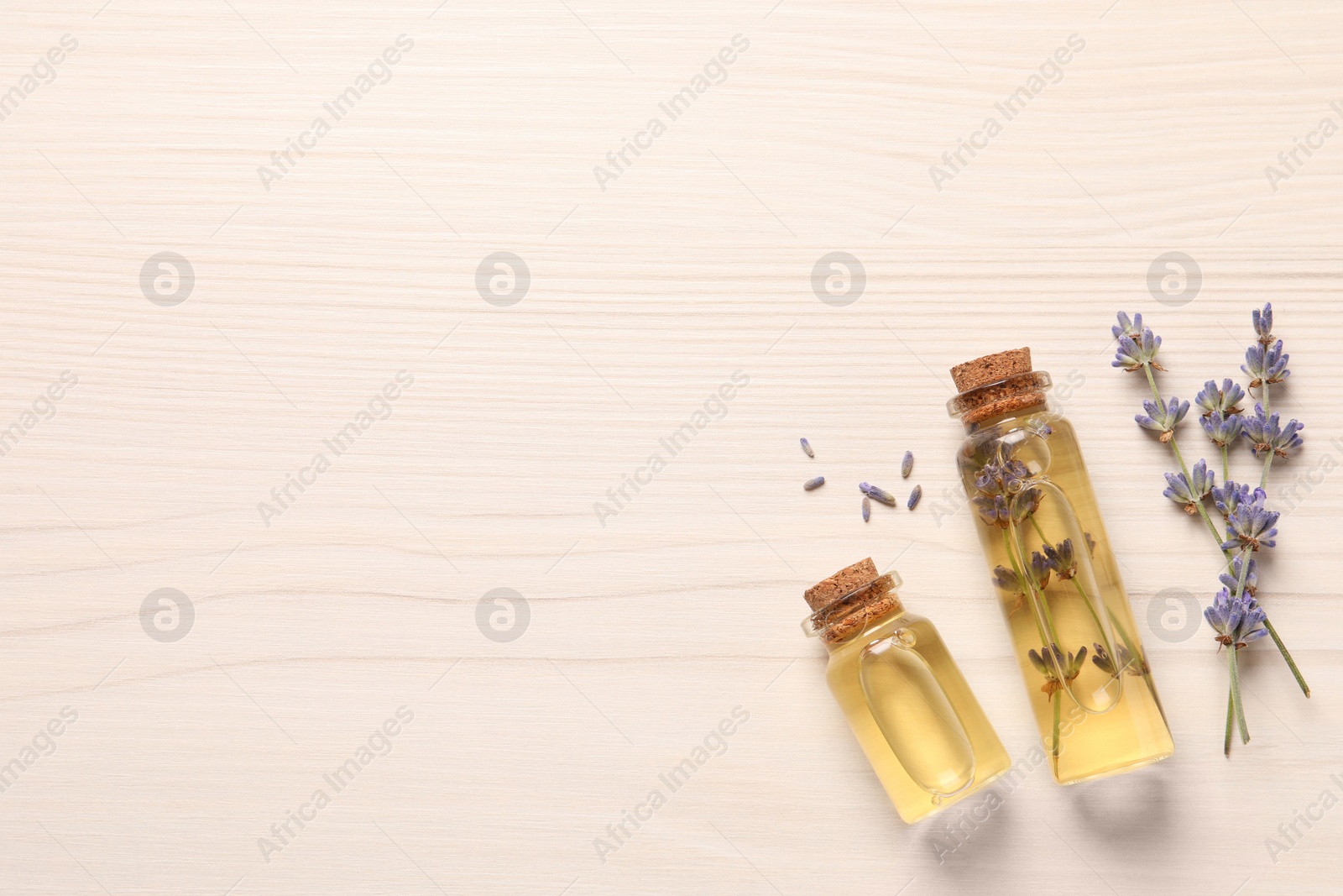 Photo of Essential oil and lavender flowers on white wooden table, flat lay. Space for text