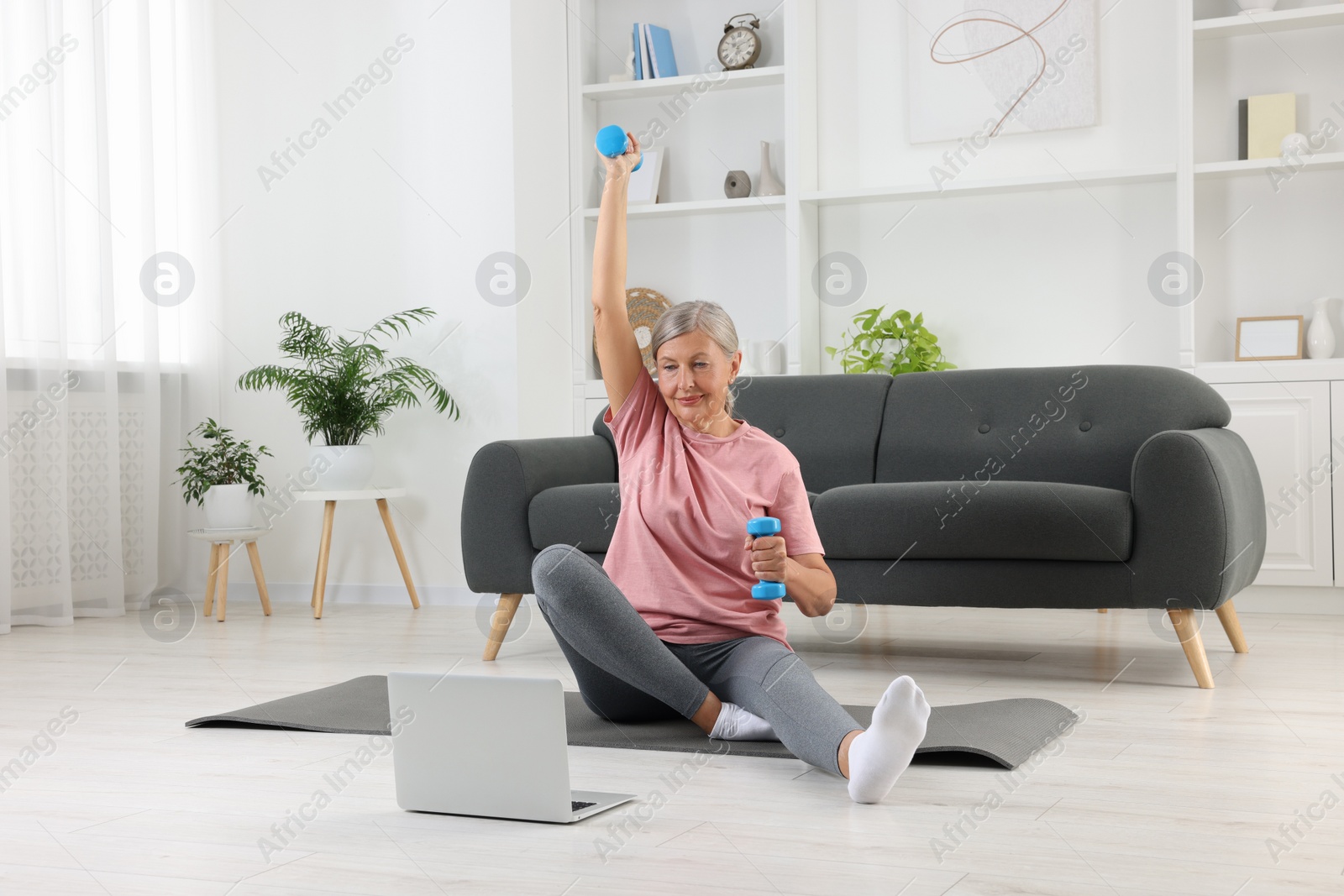 Photo of Senior woman exercising with dumbbells while watching online tutorial at home. Sports equipment