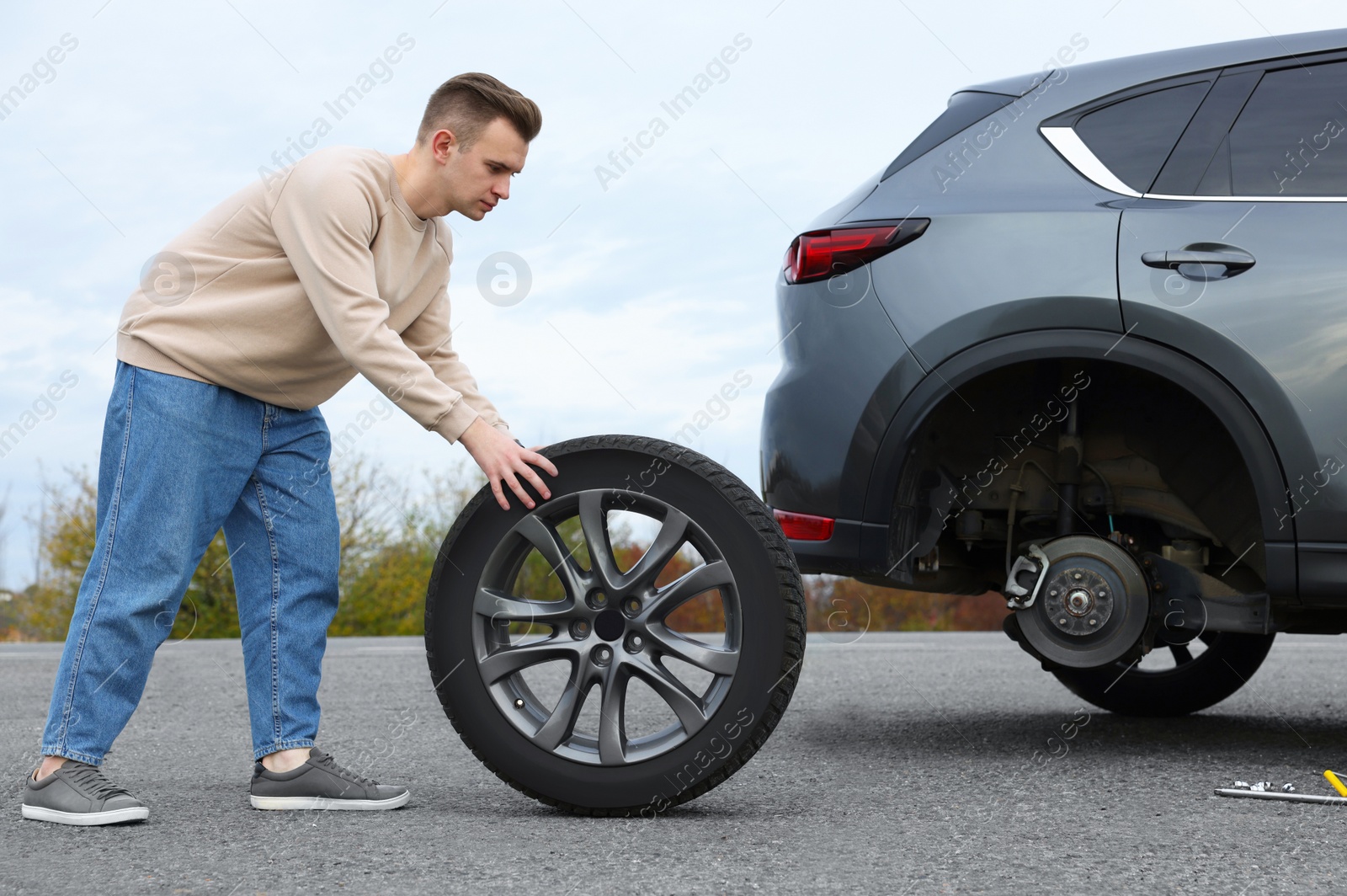 Photo of Young man changing tire of car on roadside