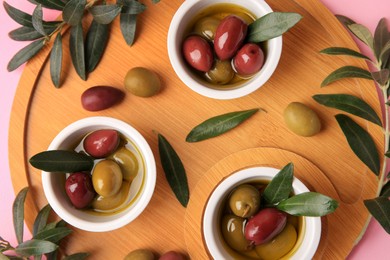 Wooden tray with different ripe olives and leaves on pink background, flat lay