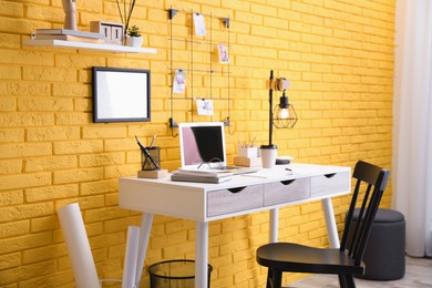 Stylish home office interior with comfortable workplace near yellow brick wall